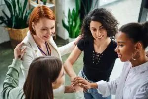 Psychologist and diverse group of multiethnic women joining hands during motivation coaching, moral support and mental wellness.