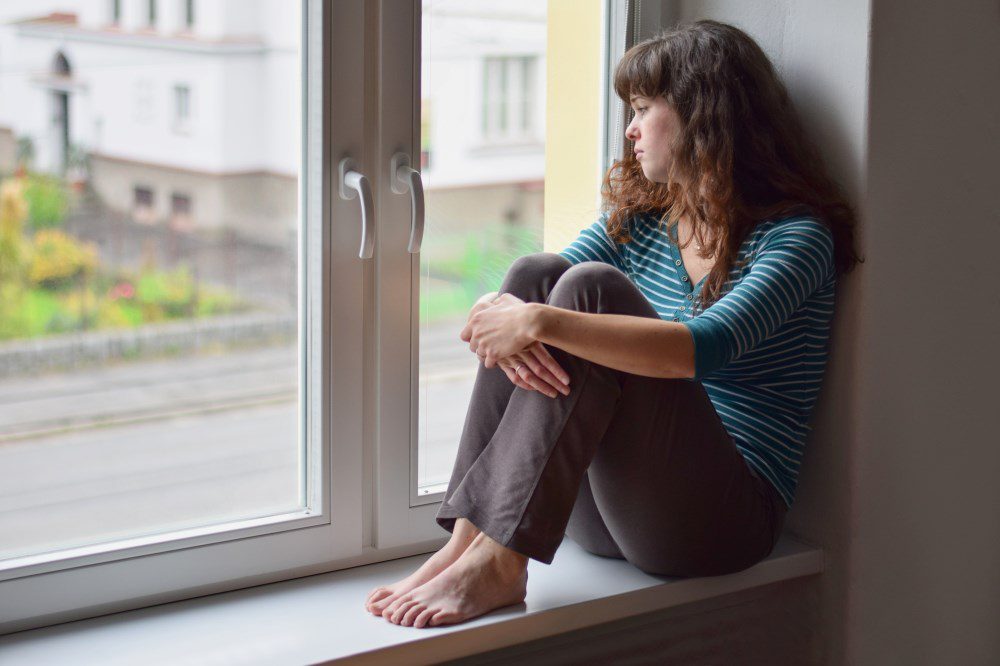 A woman looking out her window and struggling with anxiety and feelings of isolation.