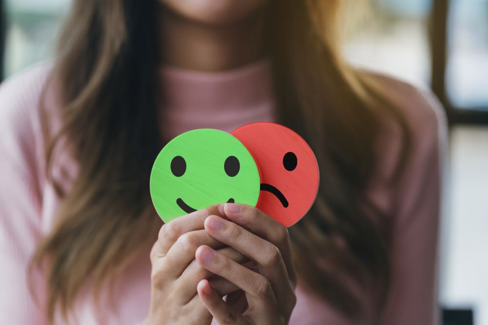 A woman holding up paper smiley faces to signify the highs and lows of Bipolar Disorder.