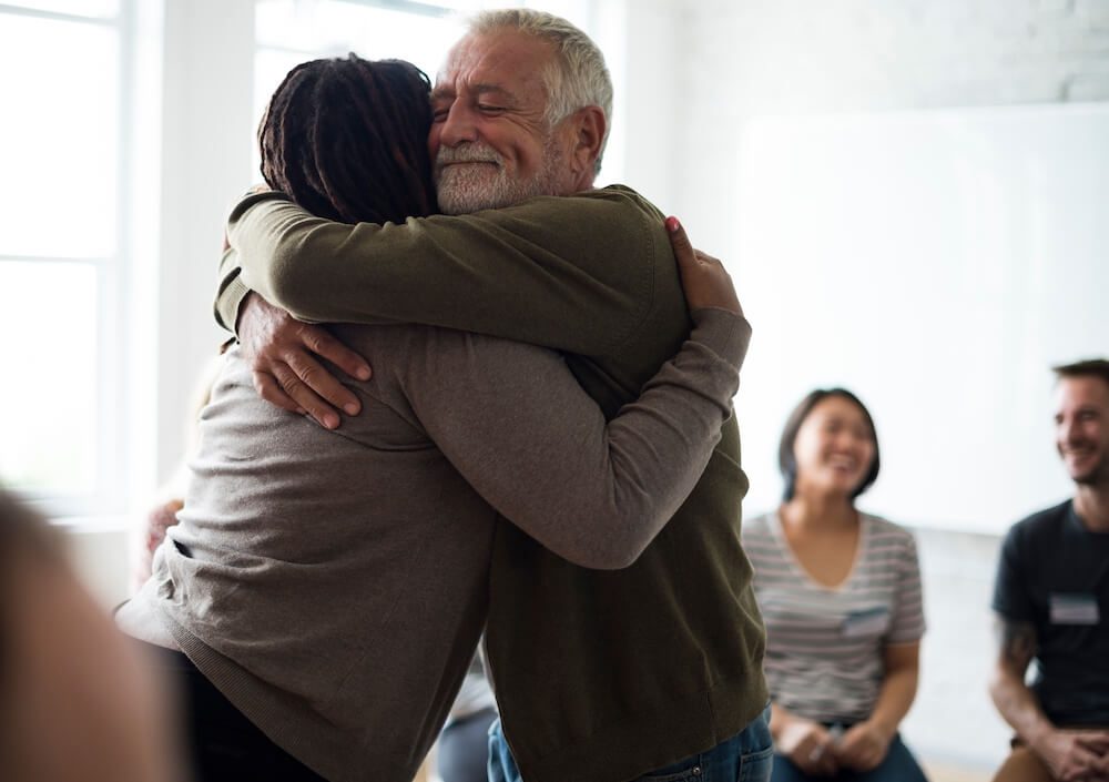 woman and man hugging during therapy session with people laughing in the background