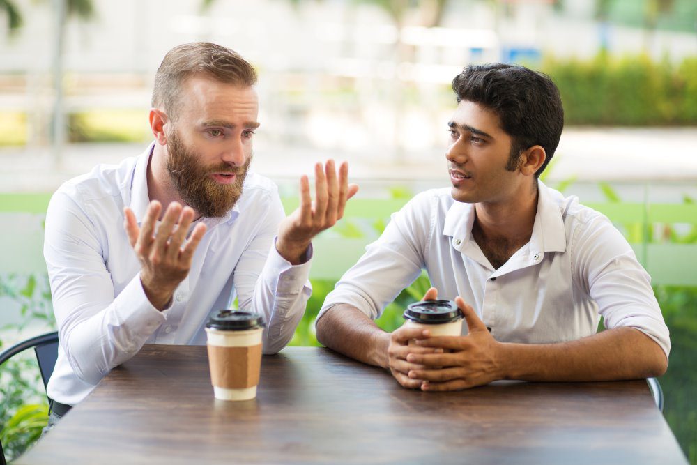 Two men discussing how their day has been while enjoying a cup of coffee.