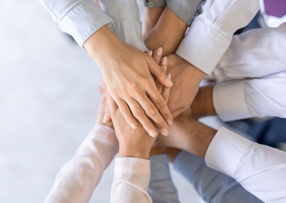 A group of professionals putting their hands together to signify that they are encouraging teamwork and collaboration.