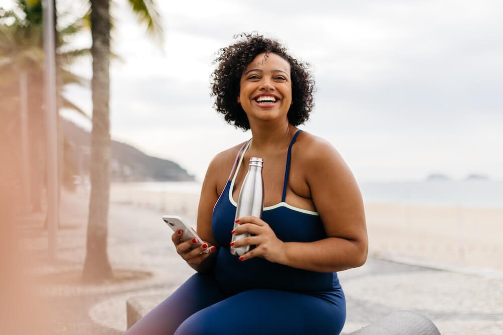 woman exercising on the beach after being diagnosed with depression laughing and drinking water
